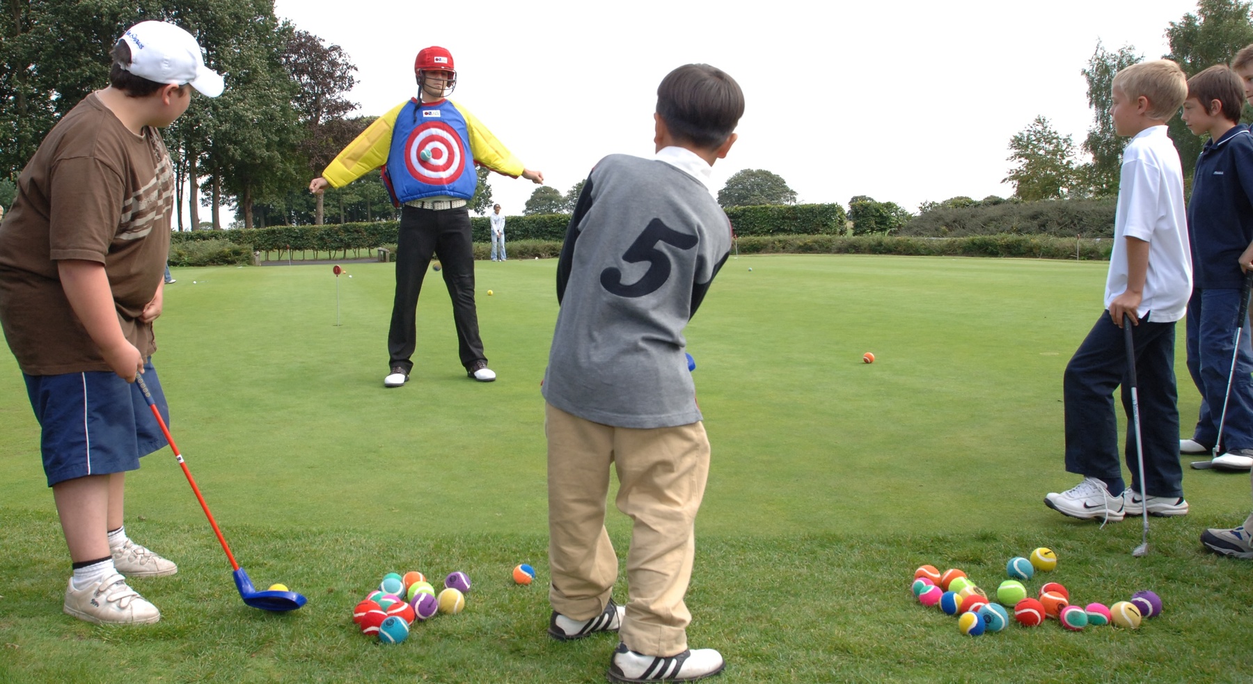 Children learning the fundamentals of golf through TriGolf – a fun and easy way for children to learn golf, using colourful plastic clubs and foam balls with various games involving targets and hoops denoting golf holes – at Hoebridge Golf Centre, Woking.