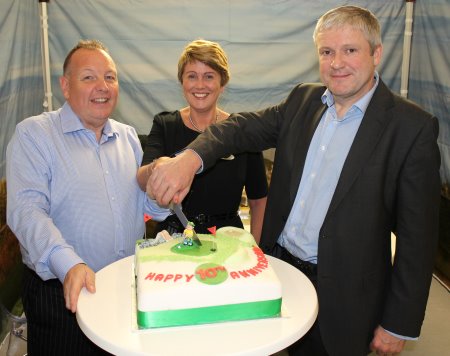 TGI Golf Managing Director Eddie Reid (left) cuts at commemorative 10th anniversary cake presented to the group by Harrogate International Centre Director Simon Kent (right) and Deborah Rolph, HIC Event Planner (centre).