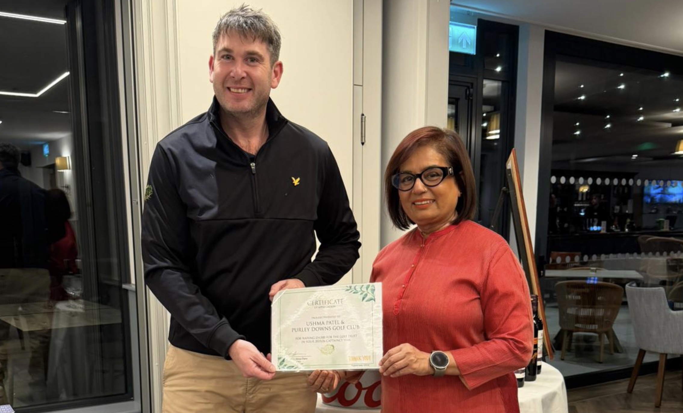 Ushma Patel, Lady Captain of Purley Downs Golf Club, hands over a cheque to Cae Menai-Davis, founder of The Golf Trust